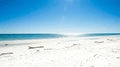 Beach day scene, bright daylight, ocean view with sun glare reflecting on water and sand.