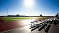 Field sports scene, bright daylight, stadium bleachers and running track beside a green field.